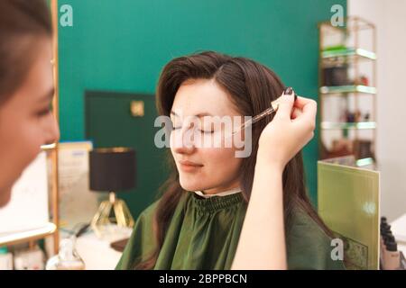 Make-up Künstler Anwendung kosmetisches Öl auf Gesicht der jungen Frau. Aufbringen von Make-up-Flüssigkeit Foundation Stockfoto