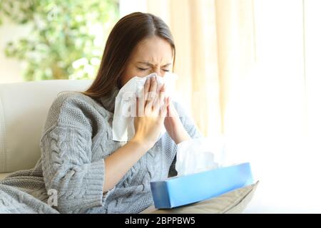 Frau bläst in ein Tuch leiden Grippesymptome sitzen auf einem Sofa zu Hause im winter Stockfoto