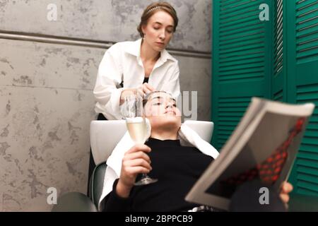 Junges Mädchen entspannt in einem Schönheitssalon mit einem Glas Champagner beim Waschen der Haare Stockfoto