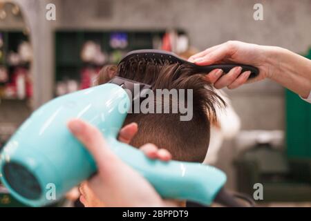 Friseur trocknet Haare von stilvollen Mann. Junge gutaussehende Kerl tun Haar Styling bei einem Friseur Stockfoto