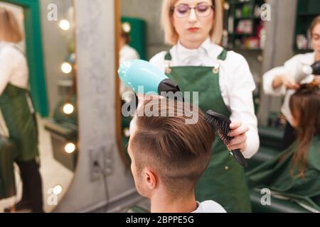 Friseur trocknet Haare von stilvollen Mann. Junge gutaussehende Kerl tun Haar Styling bei einem Friseur Stockfoto