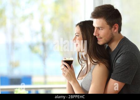 Seitenansicht Porträt eines nachdenklichen Paar oder Ehe umarmen und Blick nach draußen durch ein Fenster eines Hotels oder zu Hause mit dem Meer in der hintergrou Stockfoto