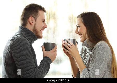 Seitenansicht Portrait von einem glücklichen Paar in Liebe einander in einer regnerischen Tag der Winter zu Hause suchen Stockfoto