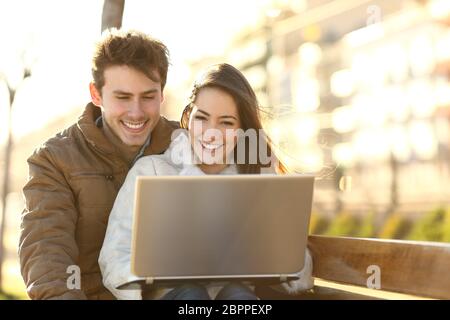 Smiley Paar beobachten Medieninhalte in einem Laptop sitzen auf einer Bank in einem Park Stockfoto