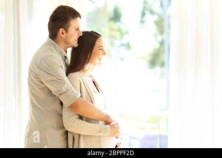 Seitenansicht Porträt einer schwangeren Frau und Ehemann, die durch ein Fenster zu Hause stehend Stockfoto