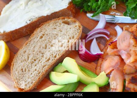 Zutaten für einen Hausgemachten geräucherten Lachs Sandwich mit Salat, rote Zwiebel, Avocado, Brot und Fische, geräuchert Stockfoto