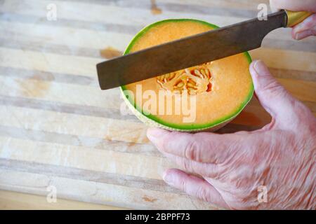 Senior schneidet in frische Melone Hälfte auf Schneidebrett mit Raum für Text Stockfoto