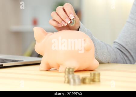 Nahaufnahme einer Frau Hand eine Münze in ein Sparschwein auf einem Tisch Stockfoto