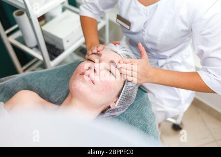 Arzt Kosmetikerin macht kosmetische Gesichtsmassage. Frau entspannt sich auf einem Kosmetikstuhl Stockfoto