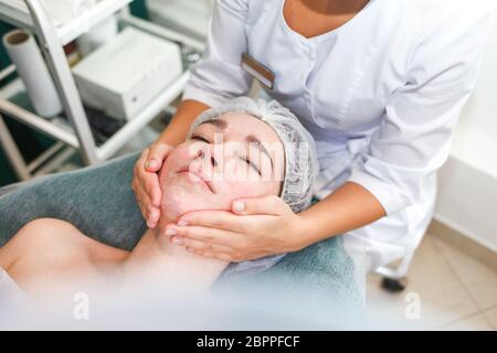 Arzt Kosmetikerin macht kosmetische Gesichtsmassage. Frau entspannt sich auf einem Kosmetikstuhl Stockfoto