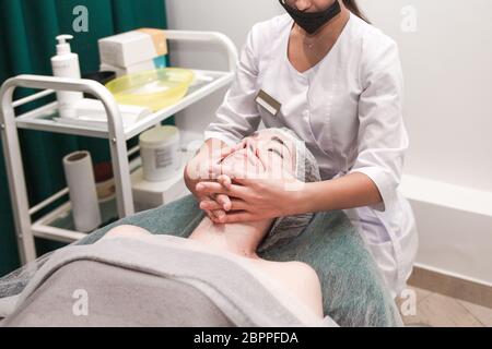 Arzt Kosmetikerin macht kosmetische Gesichtsmassage. Frau entspannt sich auf einem Kosmetikstuhl Stockfoto