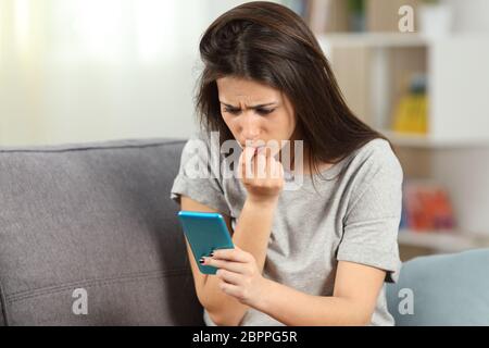 Nervös Mädchen Beißen Nägel lesen Telefon Inhalt auf einer Couch im Wohnzimmer zu Hause sitzen Stockfoto