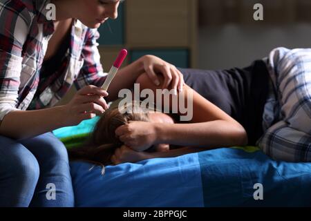 Schwester beruhigend zu einem schwangeren Teenager, der traurig ist Jammern auf dem Bett in Ihrem Schlafzimmer mit einem dunklen Licht im Hintergrund Stockfoto