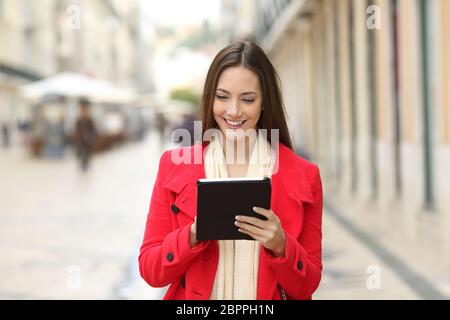 Vorderansicht Portrait Of Happy coman Kontrolle Tablette Inhalt zu Fuß auf der Straße Stockfoto