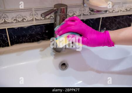 Eine Hand in einem rosa Handschuh wäscht ein Waschbecken im Badezimmer mit einem Schwamm mit Schaumwaschmittel. Reinigungsfirma reinigt das Haus. Desinfektion des Stockfoto
