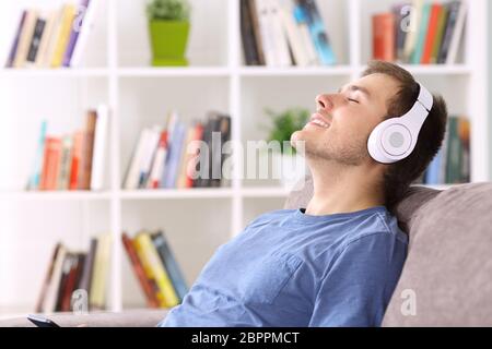 Seitenansicht Porträt eines Mannes, der sich zu Hause auf einer Couch entspannt und Musik mit Kopfhörern hört Stockfoto