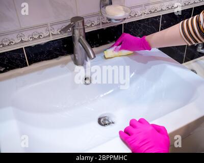 Eine Hand in einem rosa Handschuh wäscht ein Waschbecken im Badezimmer mit einem Schwamm mit Schaumwaschmittel. Reinigungsfirma reinigt das Haus. Desinfektion des Stockfoto