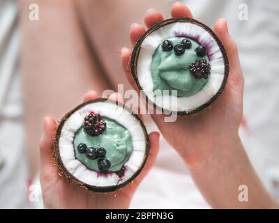 Zwei coconut Hälfte mit Smoothie oder Joghurt in der Frau die Hände. Blue spirulina Smoothie in Kokosnuss mit gefrorenen Beeren. Gesundes Frühstück Konzept. Ideen und Stockfoto