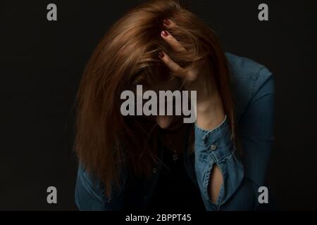 Low Key Porträt der jungen Frau in Schwierigkeiten sitzen und hielt sie neigte den Kopf. Stockfoto