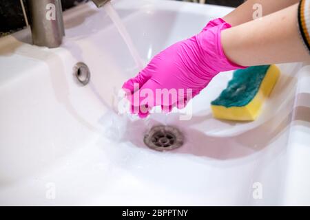 Eine Hand in einem rosa Handschuh wäscht ein Waschbecken im Badezimmer mit einem Schwamm mit Schaumwaschmittel. Reinigungsfirma reinigt das Haus. Desinfektion des Stockfoto