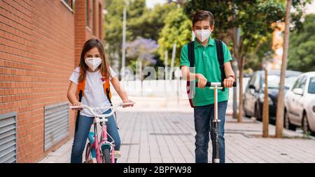 Junge und Mädchen tragen Masken und fahren einen Roller und Fahrrad auf der Straße Stockfoto