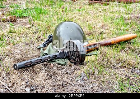 Ein Helm und eine Maschinenpistole aus der Zeit des Großen Vaterländischen Krieges, ein Beutel der schützende Farbe vor dem Hintergrund der Gras Stockfoto