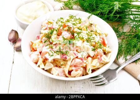 Salat von Crab Sticks, Käse, Knoblauch, Eier und Tomaten, gekleidet mit Mayonnaise in einer Platte, Serviette und Petersilie auf einem Holzbrett Hintergrund Stockfoto