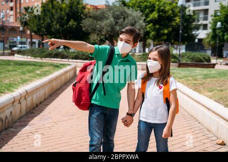 Junge und Mädchen mit Rucksäcken und Masken gehen zur Schule in Coronavirus Pandemie Stockfoto