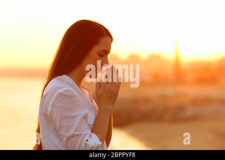 Profil von einer konzentrierten Frau mit Händen gemeinsam beten bei Sonnenuntergang Stockfoto