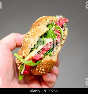 Mans Hand eine Rote Beete und Rucola Burger mit fehlenden beißt. Stockfoto