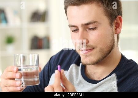 Ein ernsthafter Mann, der bereit ist, eine Pille zu nehmen, die zu Hause auf einer Couch sitzt Stockfoto