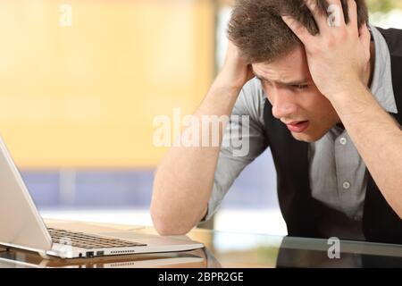 Nahaufnahme eines besorgt Unternehmers gerade Laptop mit den Händen auf dem Kopf sitzen in einem Schreibtisch in einem Büro indoor Stockfoto