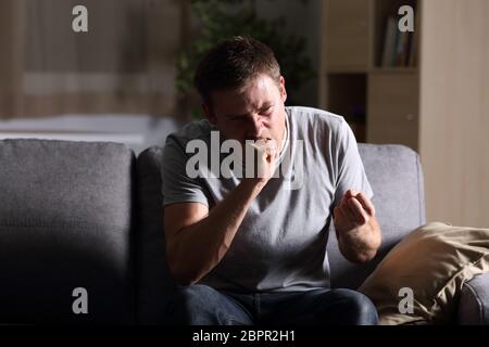 Vorderansicht Portrait von einem wütenden Mann zu Hause in der Dunkelheit auf einem Sofa zu Hause sitzen Stockfoto