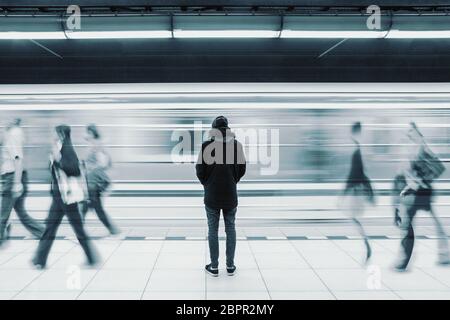 Lange Belichtung Bild mit einsamen Jungen Mann erschossen, von hinten an der U-Bahn station mit verschwommenen fahrenden Zug und nur wenige Leute im Hintergrund Stockfoto