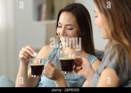 Frauen werfen Würfel Zucker in Kaffee auf einer Couch im Wohnzimmer zu Hause sitzen Stockfoto