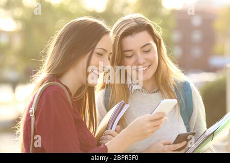 Zwei schöne Studenten beobachten Medieninhalte auf Zeile in ein smart Phone im Freien in einem Park oder einer Universität campus Stockfoto