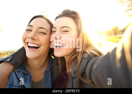 Zwei lustige Freunde unter Selfies draußen auf der Straße bei Sonnenuntergang mit einem warmen Licht im Hintergrund Stockfoto