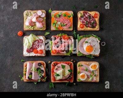 Satz von acht verschiedenen Sandwiches mit Fleisch in quadratische Form. Top View oder flach. Sortiment Fleisch Toast auf schwarzem Hintergrund. Idee, kreative Konzept Stockfoto
