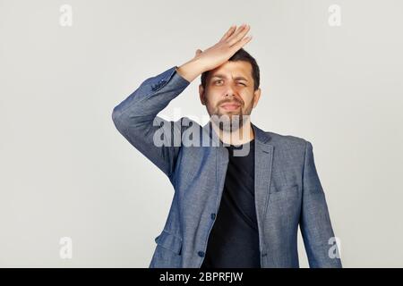 Junger Geschäftsmann, der seine Hand auf der Stirn auflegt, sich an etwas wichtiges erinnert, vergisst er auf einem grauen Hintergrund. Ein Mann erinnert sich plötzlich an große Verkäufe in den Geschäften Stockfoto