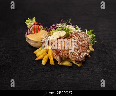 Gebratenes Schweinefleisch mit Pommes Frites und grüner Salat auf schwarzem Hintergrund hacken Stockfoto