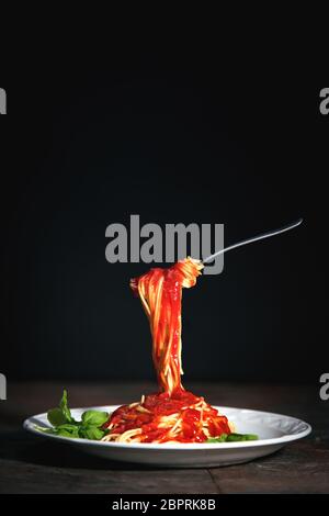 Leckere, appetitliche klassische italienische Spaghetti-Pasta mit Tomatensauce, Käse-Parmesan und Basilikum auf einem dunklen Tisch Stockfoto