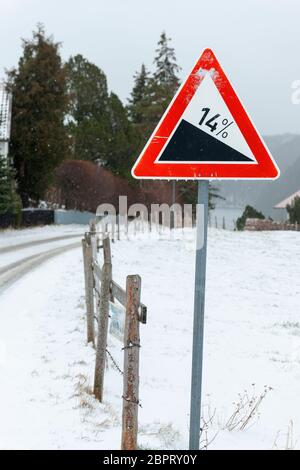 Warnschild an einem steilen Hang auf einer verschneiten Straße in Bayern im Winter. Stockfoto