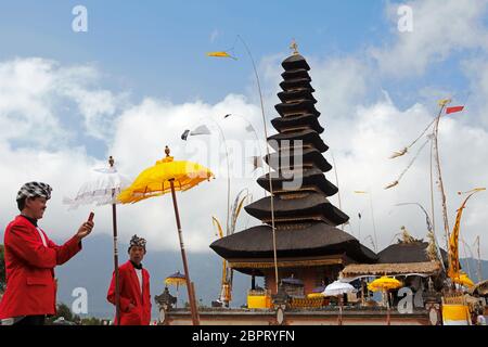 Pecalang (traditionelle balinesische Polizisten) machen eine Pause für mobile Fotosession vor dem Lingga Petak Tempel in Ulundanu Beratan, Bali, Indonesien. Stockfoto