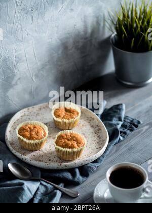 Hausgemachte Muffins für das Handwerk Teller und Tasse Kaffee über graues Holztisch. Karotte Cupcakes mit kopieren. Getonten Bild im skandinavischen Stil. Stockfoto