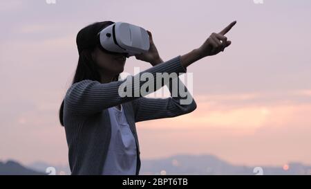 Frau benutzt eine Virtual-Reality-Brille auf dem Dach bei Sonnenuntergang Stockfoto