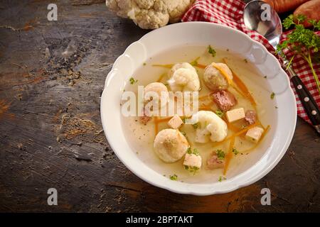 Top down Sicht auf eine Schüssel mit deutschen Frühling Suppe auf einem rustikalen Tisch mit Knochenmark Knödel, Karotten und Blumenkohl in einer Brühe mit frischen Kräutern Stockfoto