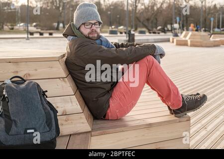 Verdächtiger Tourist schaut aufgeregt auf seinen Rucksack und fürchtet, dass er gestohlen wird, während er auf einer Bank im Park sitzt. Stockfoto