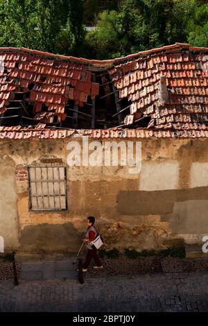 Frau, die ungestört durch das zerbröckelnde Gebäude zu ihrer Rechten in der Altstadt von Cuenca, Spanien, geht. Stockfoto