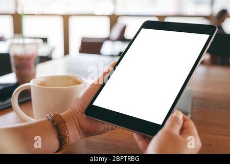 Mockup-Bild der Hände halten schwarzen Tablet-pc mit leeren weißen Bildschirm mit Kaffeetasse auf Holztisch Stockfoto