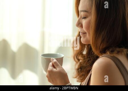 Nahaufnahme Bild einer schönen asiatischen Frau hält und riecht eine Tasse heißen Kaffee mit Gefühl entspannt am Morgen Stockfoto